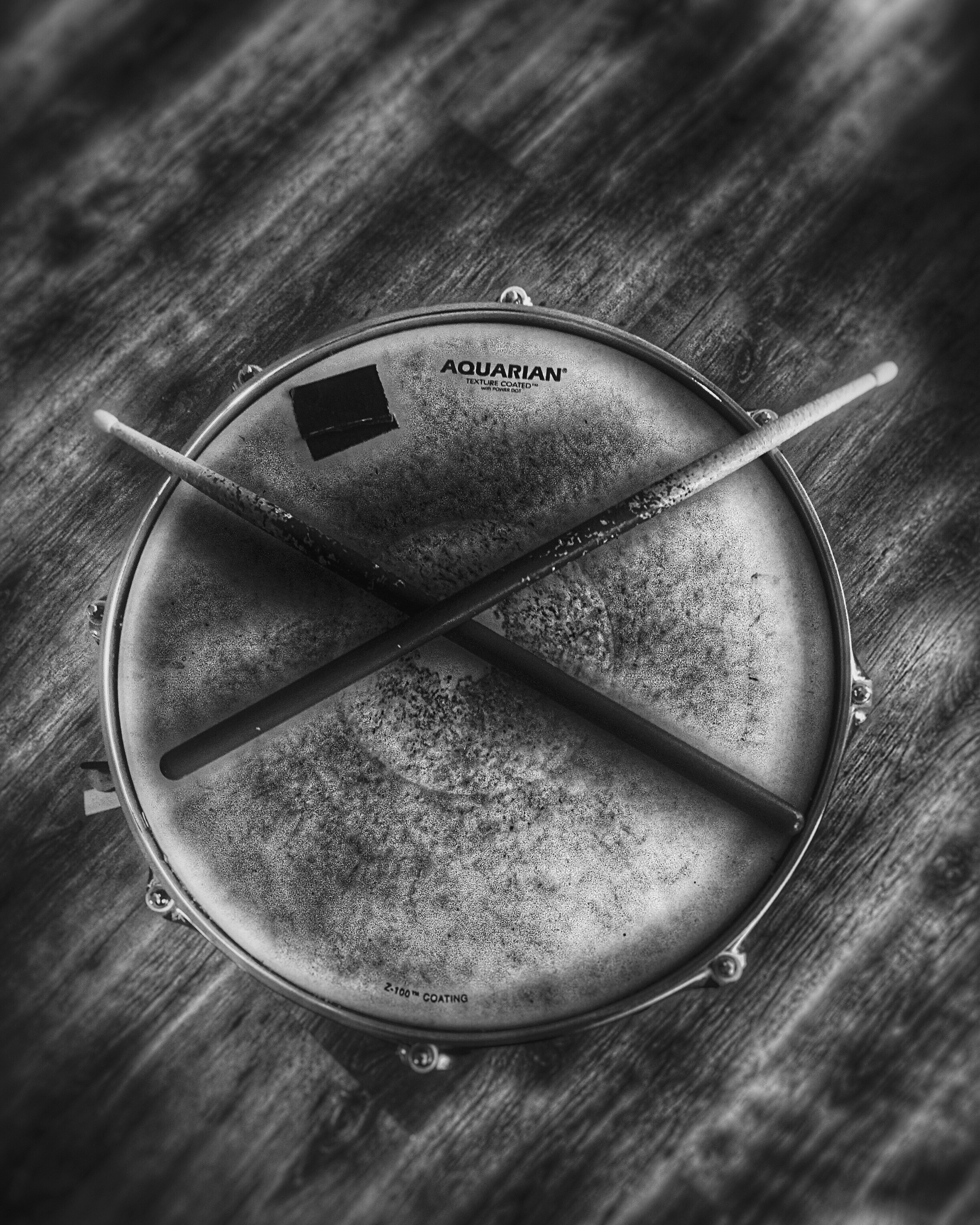 Egy Fekete-fehér fénykép, amin felülnézetből egy pergődob és rajta X alakban két dobverő látszik