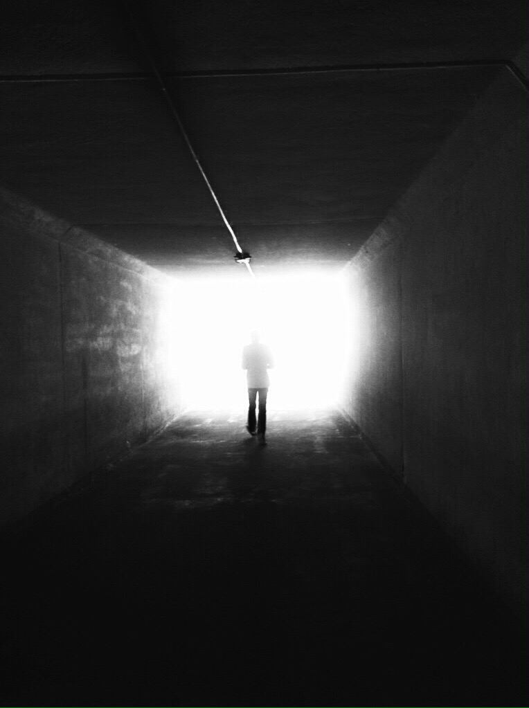 Egy alak sétál egy alagútba az éles fény felé (fekete-fehér fénykép)