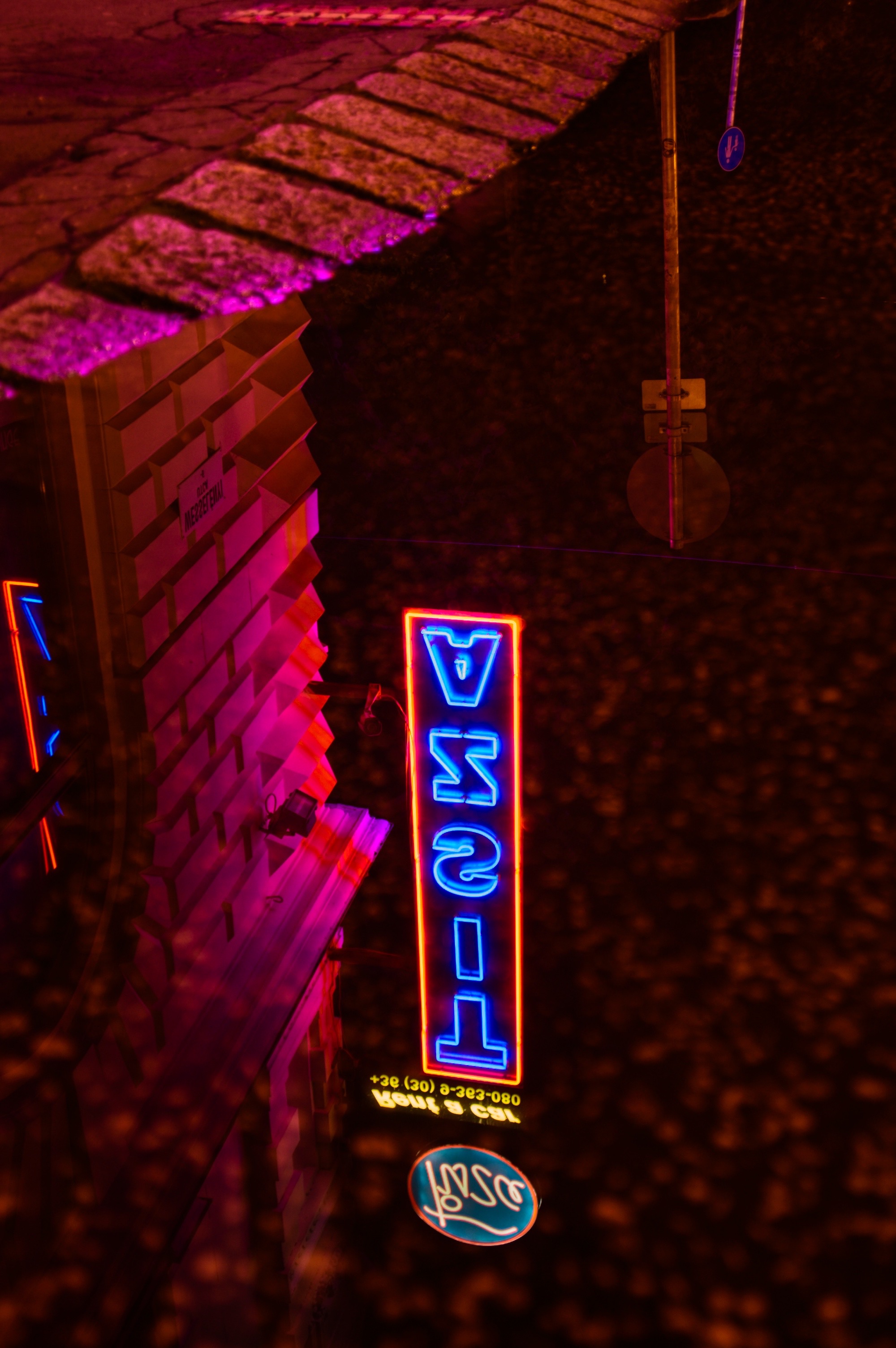 A szegedi Tisza Hotel neon feliratának tükröződése a pocsolyában