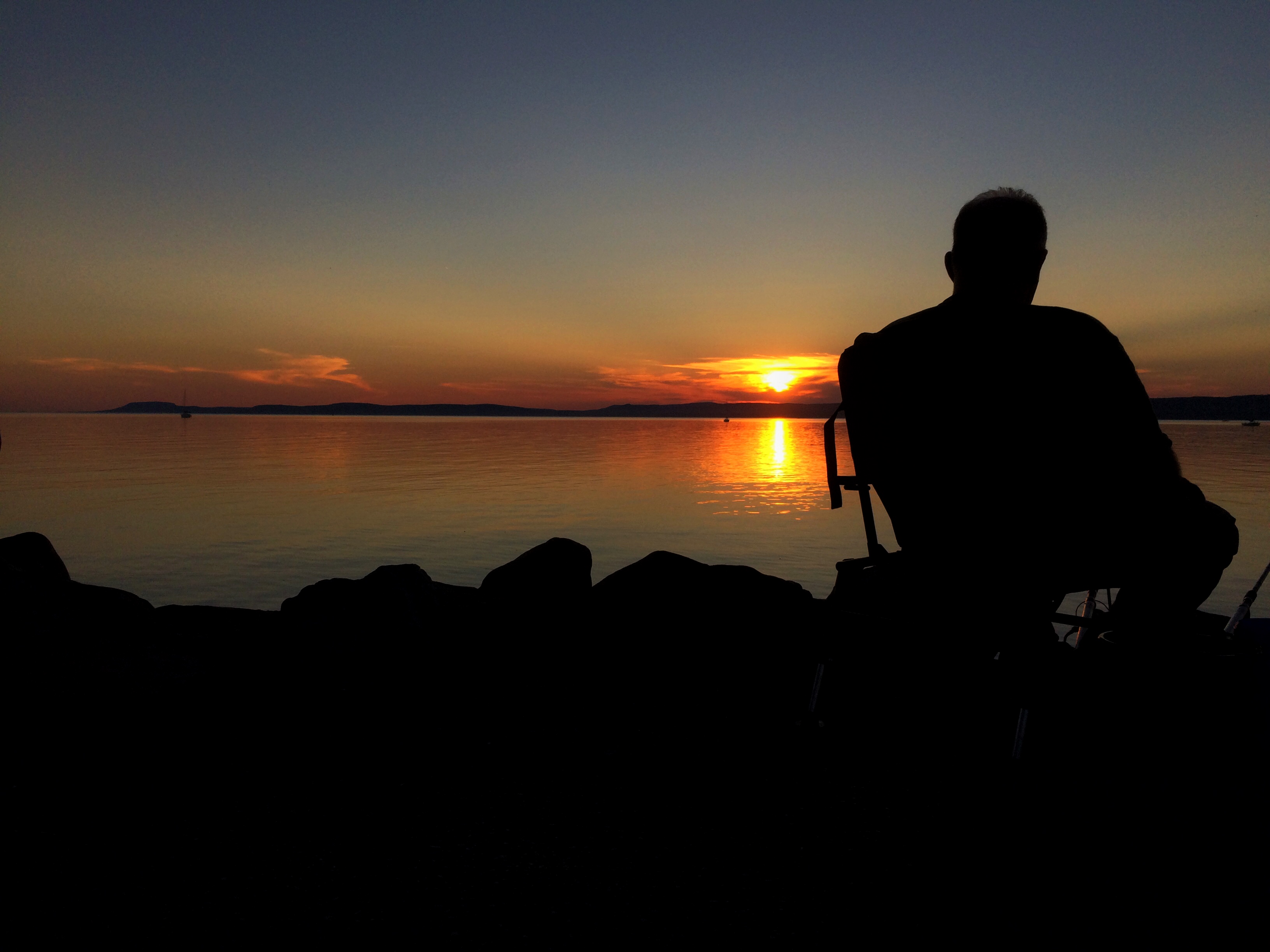 Egy magányos horgász csodálja a balatoni naplemenét